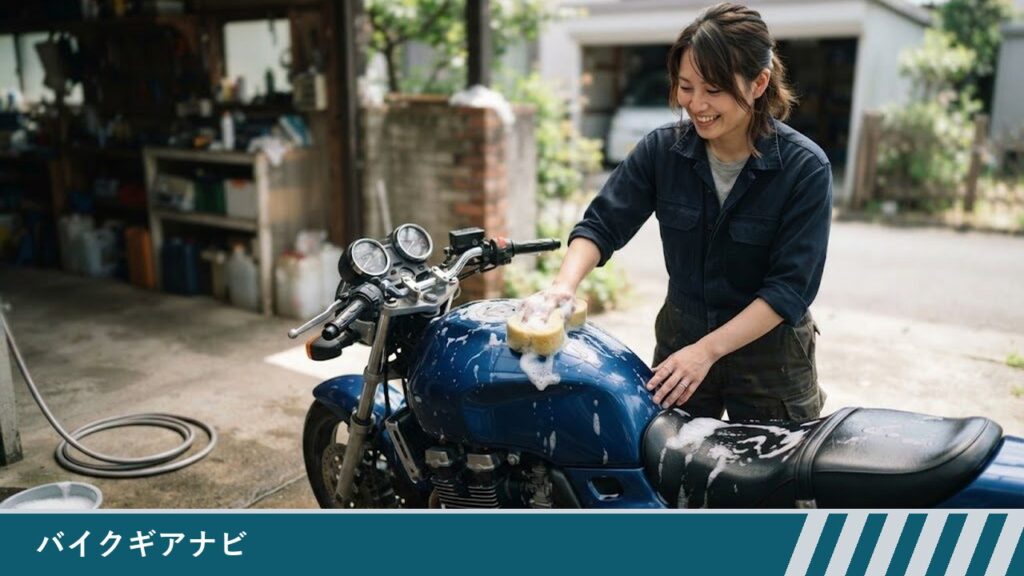 自宅の庭先で、女性が青いバイクのタンクの上面に泡をつけたスポンジを当てて洗っている様子