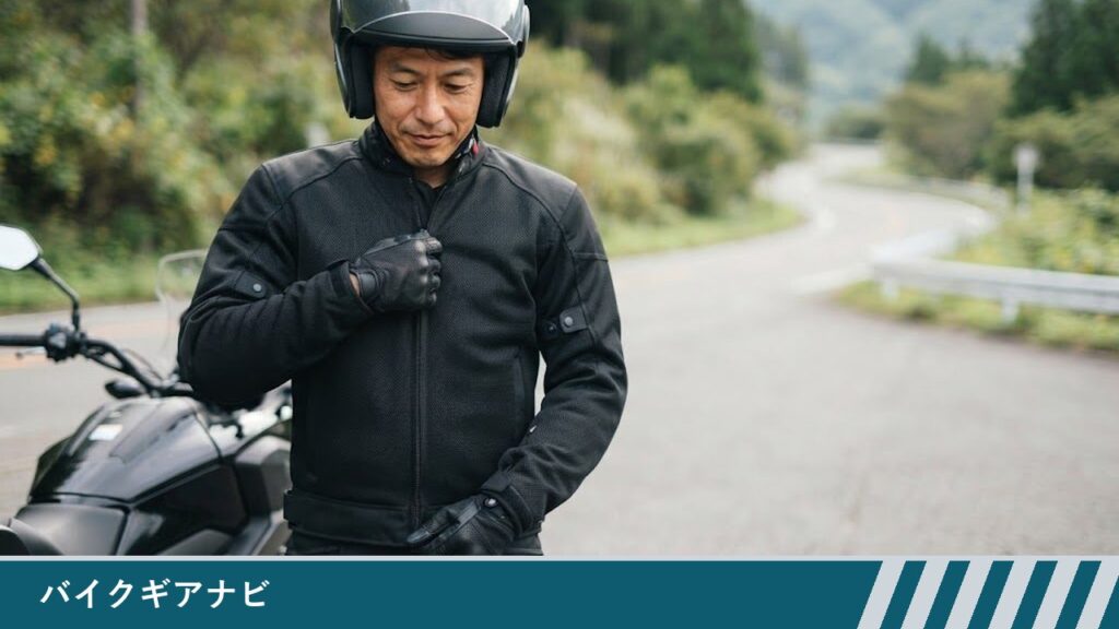 停車したバイクの横で、男性がメッシュ入りのバイクジャケットを着て前のファスナーを閉めている様子