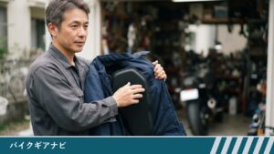 自宅のガレージ前で、男性がバイク用ジャケットの内側のポケットに背中プロテクターを入れている様子