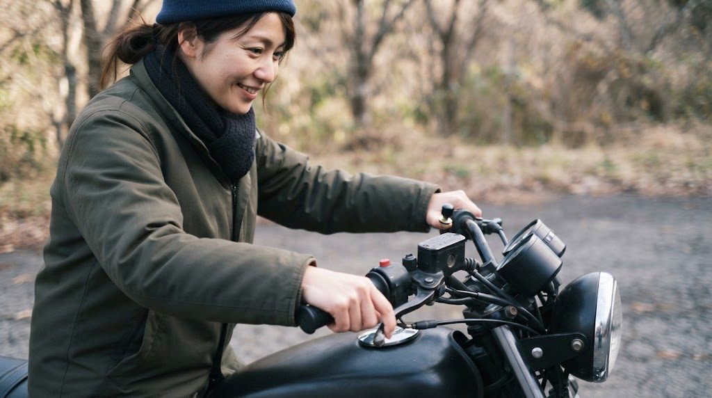 毛糸の帽子とネックウォーマーを着けた女性が、停車したバイクのハンドルのグリップに手をかけている様子