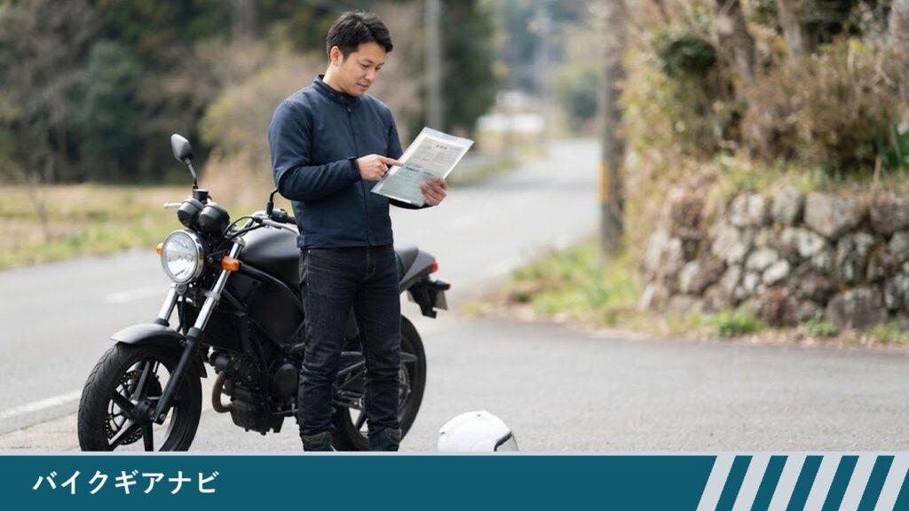 道路脇に停めたバイクの横で、男性が透明なクリアファイルに入れた書類を持ち、指でさしている様子。足元にヘルメットが置いてある