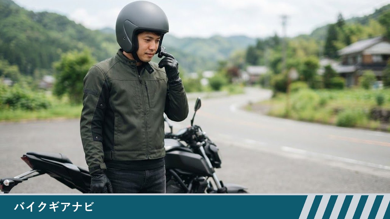 停車したバイクの横で、ヘルメットをかぶった男性が、ヘルメット側面のインカム本体をグローブをした指で操作している様子