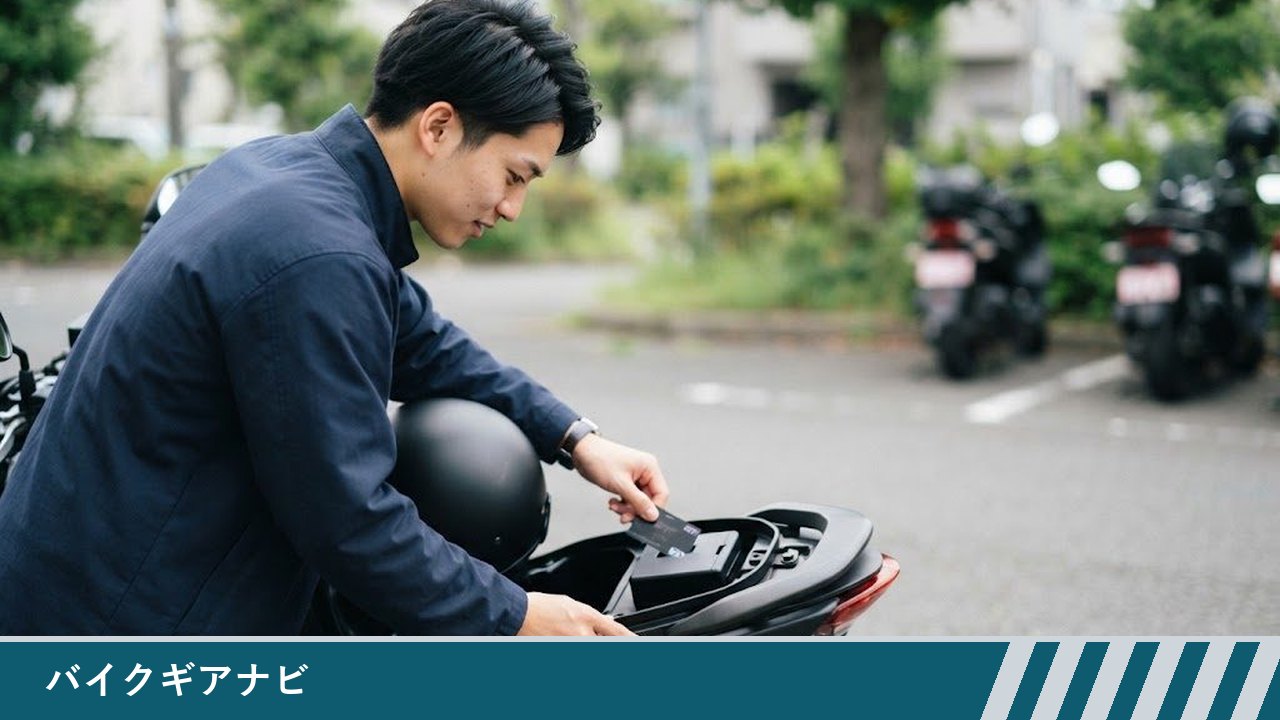 駐輪場で、若い男性がバイクのシートを開け、シート下の収納にある黒い車載器にETCカードを差し込もうとしている様子